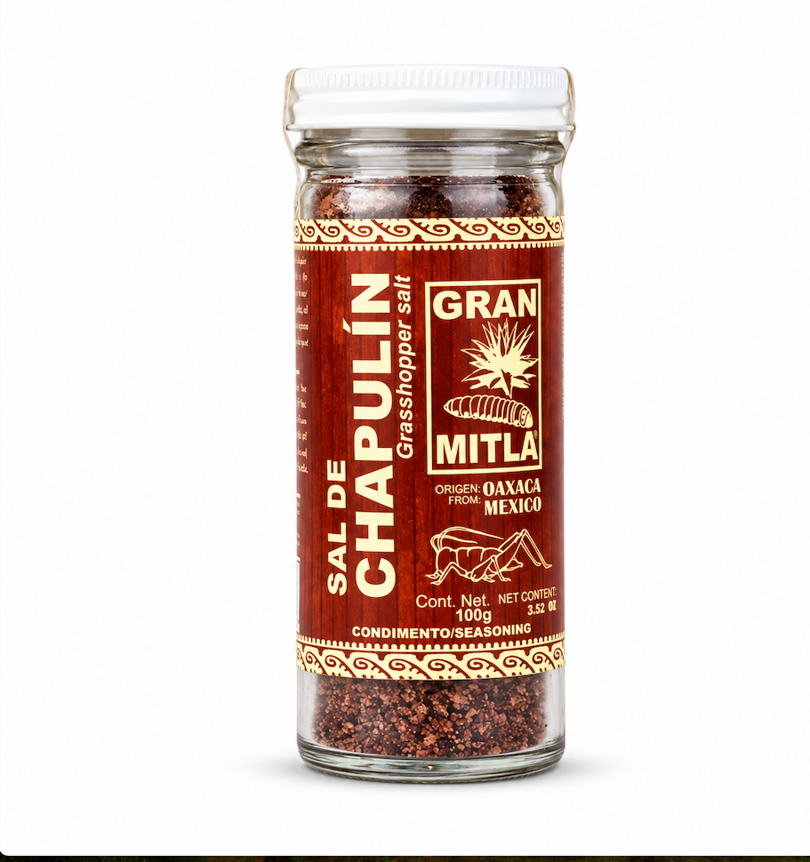 A glass jar of Mitla Gran Sal de Chapulin seasoning, featuring a white cap and a reddish-brown label with gold lettering, set against a plain white background.